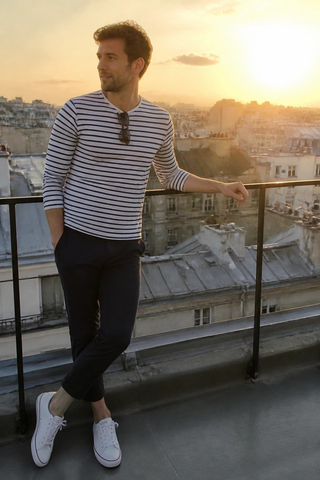 Man in striped shirt leaning on balcony overlooking city at sunset