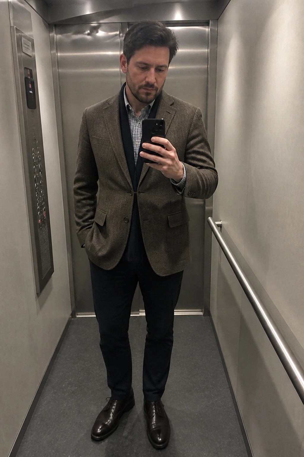 Man in brown tweed blazer holds phone while standing in elevator