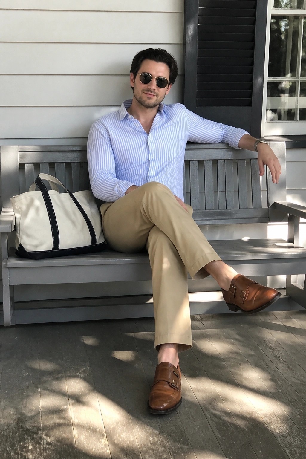 Man in striped shirt and khakis seated on gray porch bench with canvas tote bag