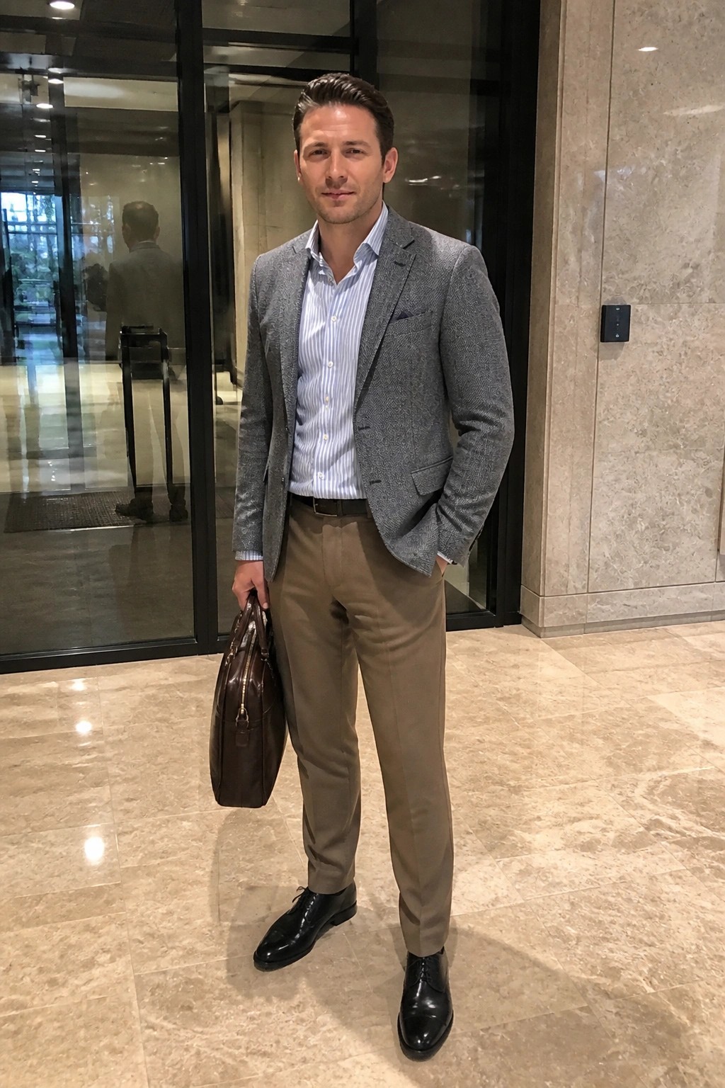 Man in gray blazer and striped shirt holds brown briefcase in marble lobby