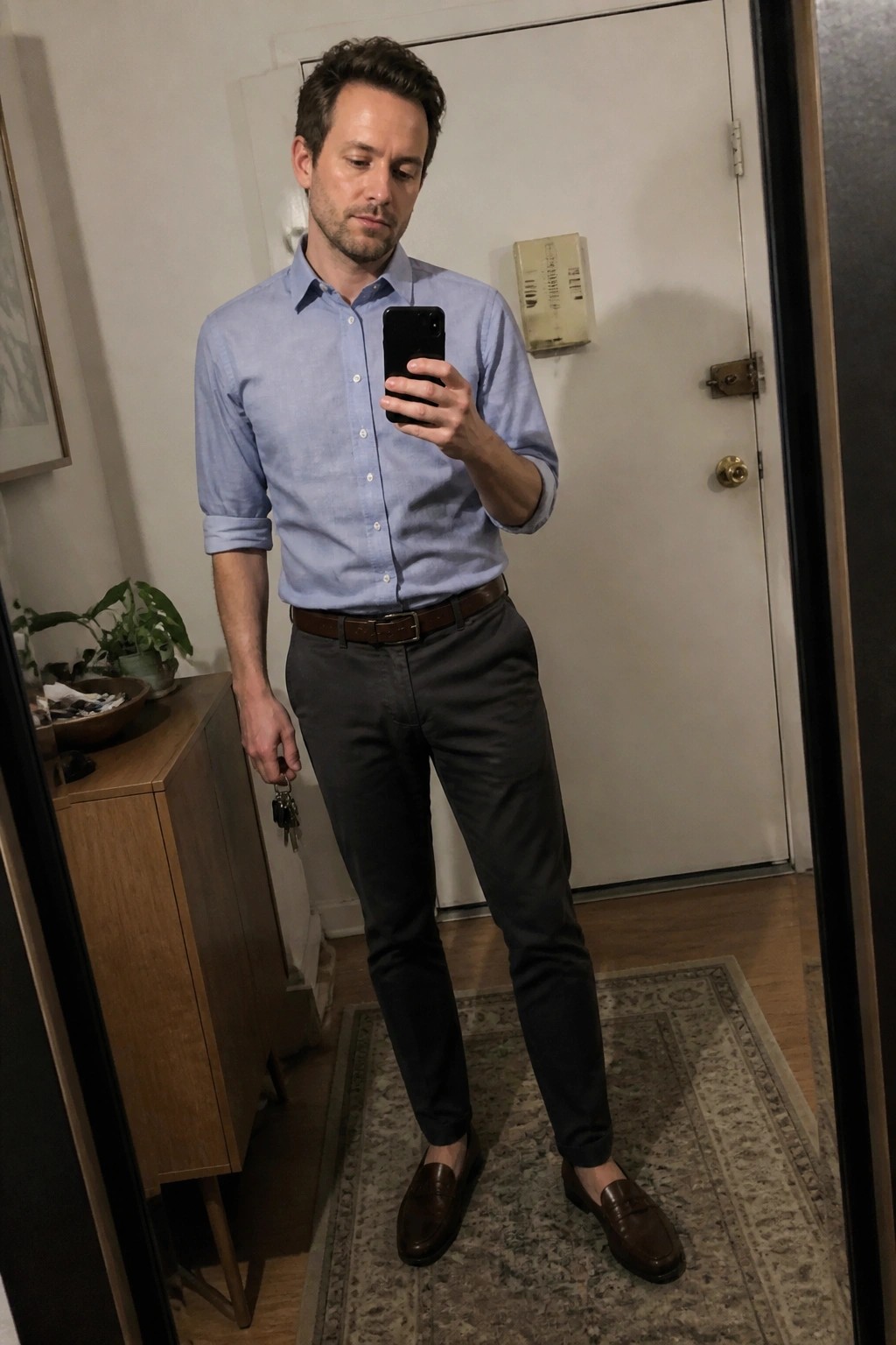 Man in light blue shirt and gray pants taking mirror selfie with phone