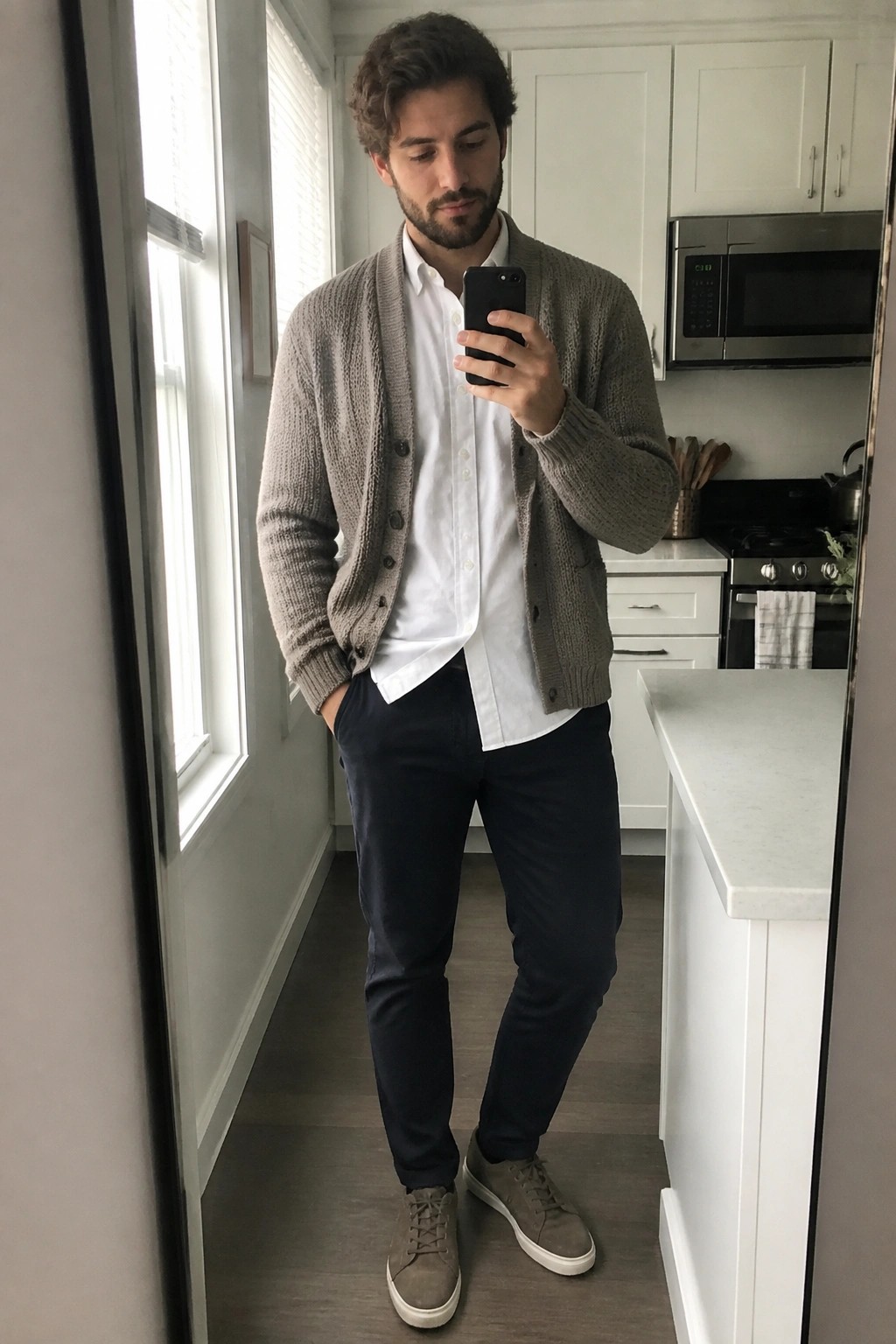 Man in gray cardigan and white shirt taking mirror selfie in kitchen
