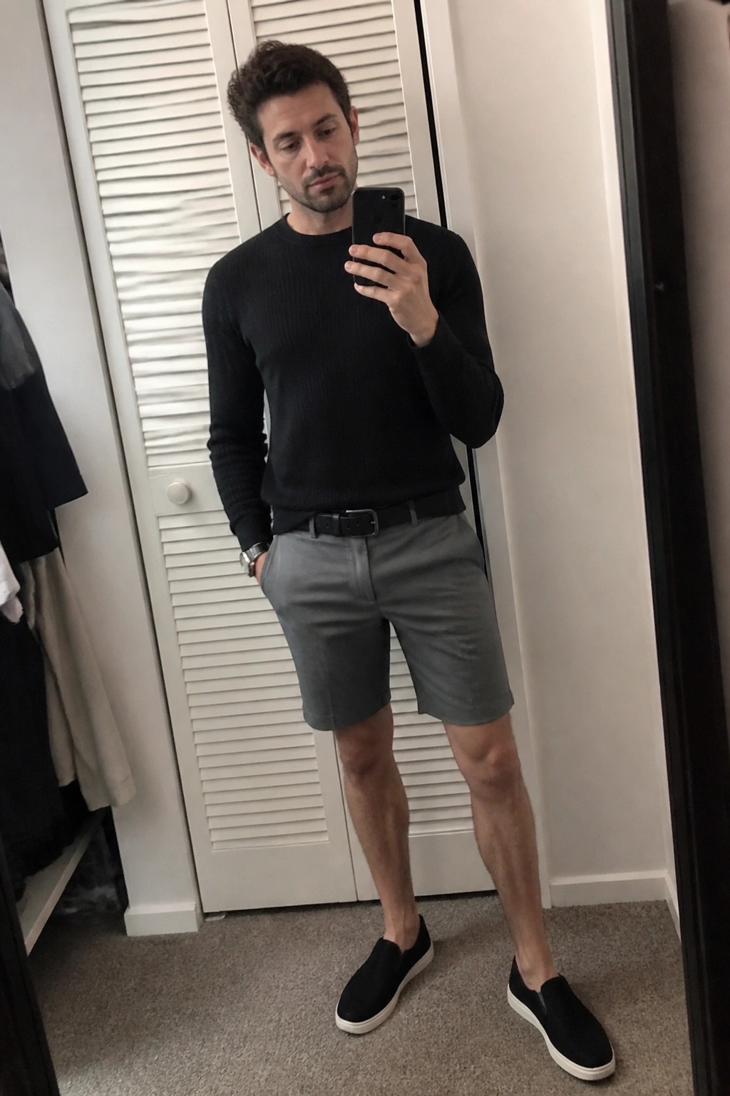 Man in black sweater and gray shorts taking mirror selfie with phone