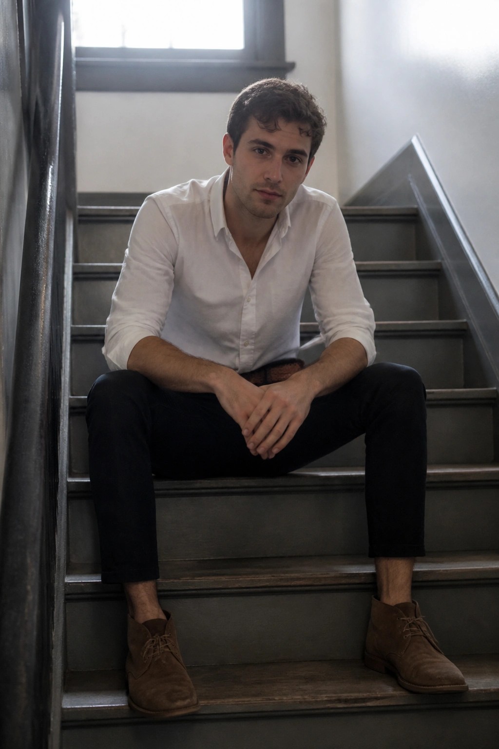 Young man in white shirt and black pants sitting on gray staircase.