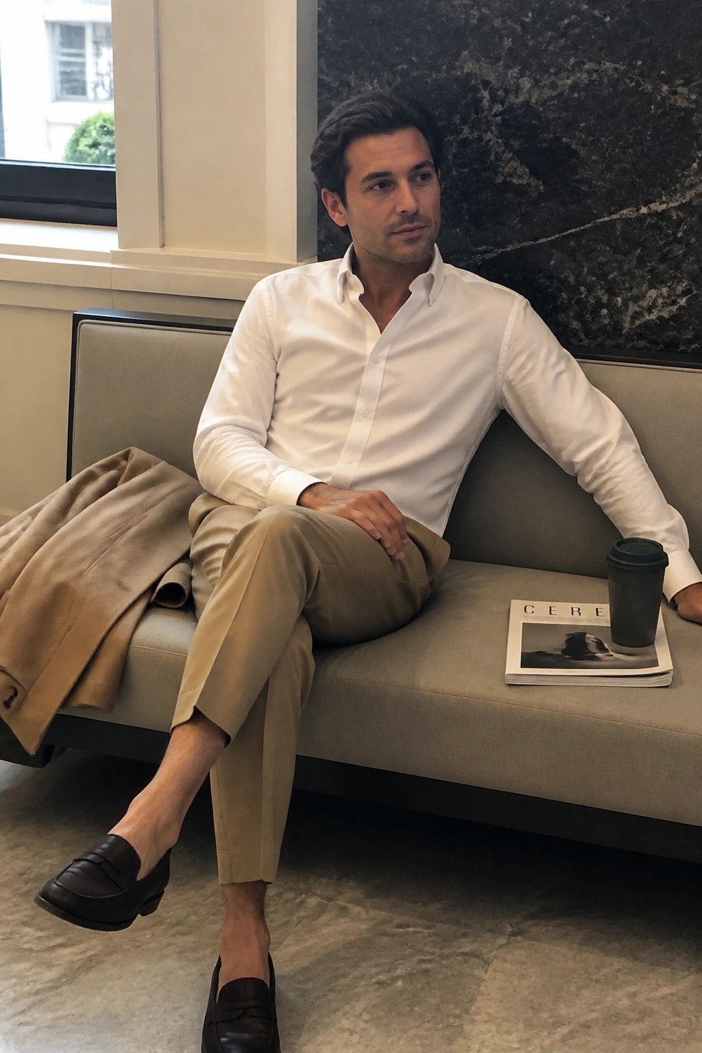 Man in white shirt and beige pants on sofa beside magazine and coffee cup