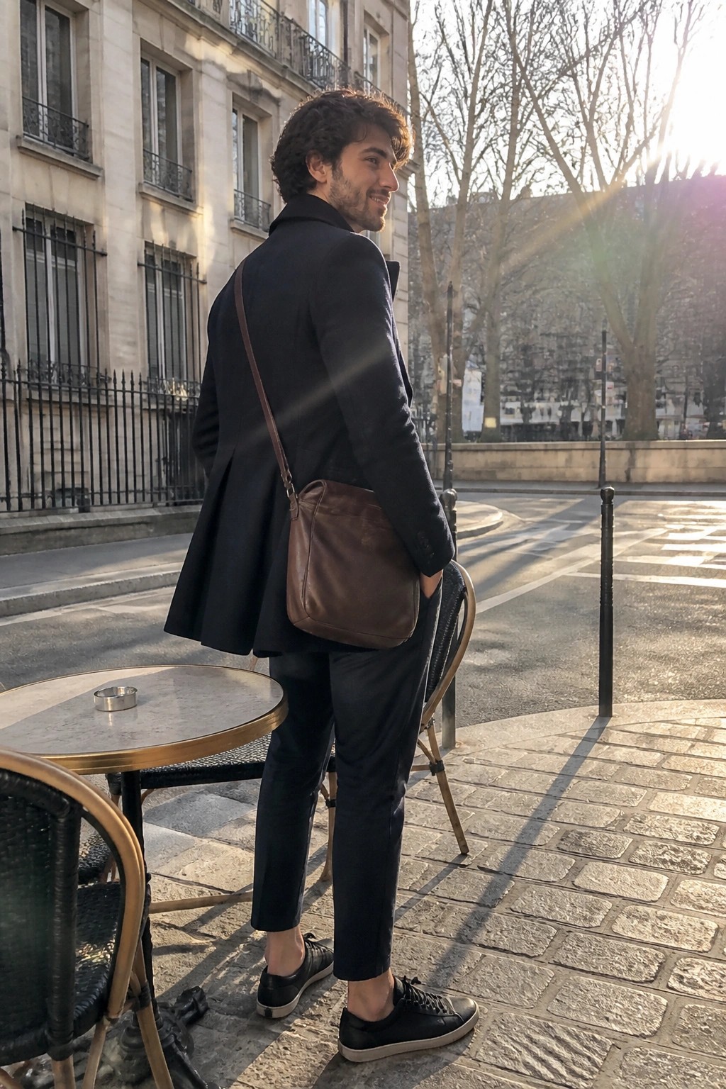 Man in dark suit with brown leather bag beside cafe table on sunny street