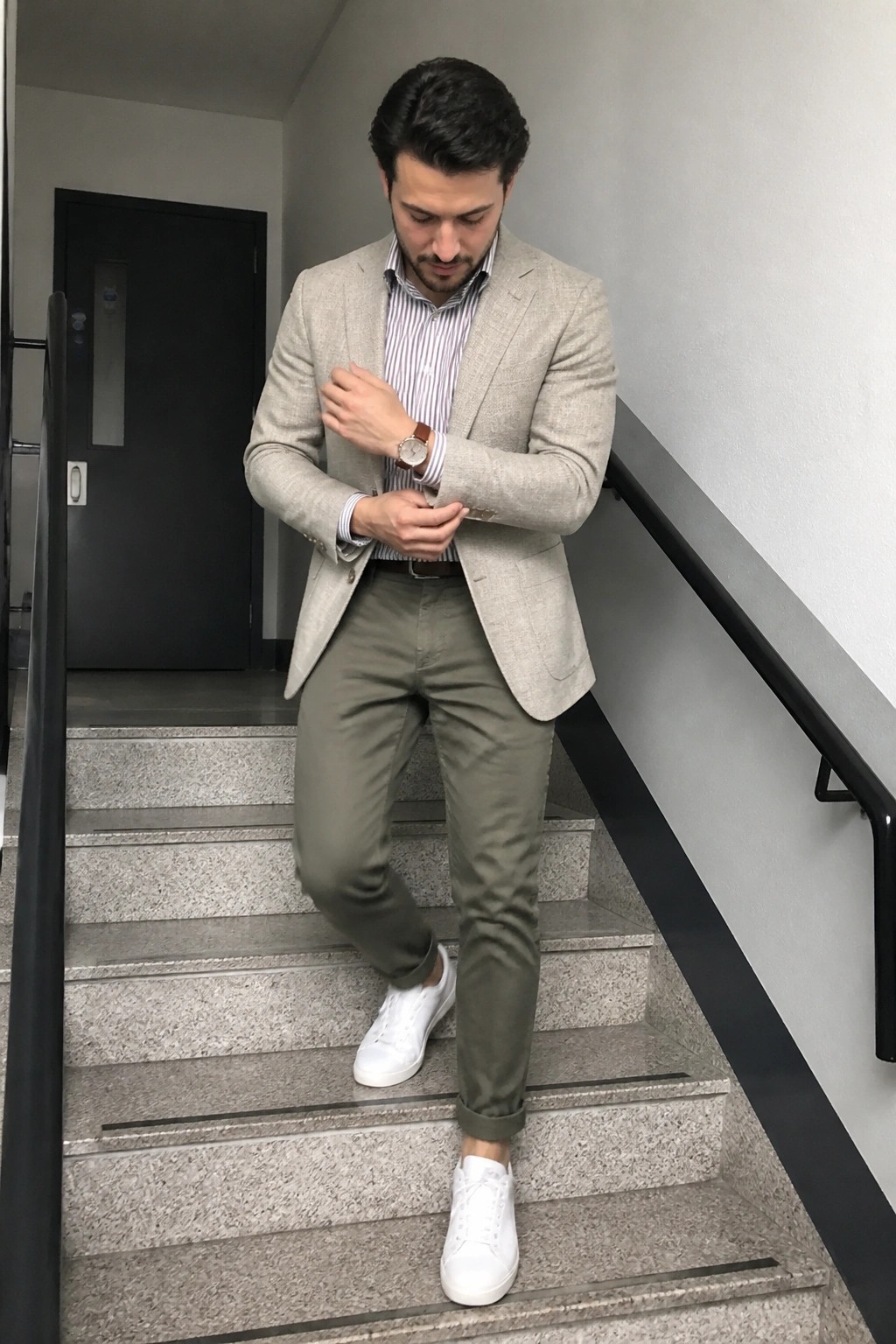 Man in beige blazer and olive pants adjusts cuff on stairs