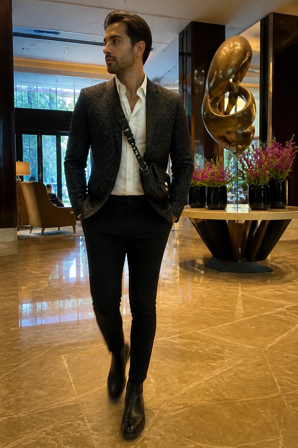 Man in patterned blazer over white shirt with black crossbody bag in luxury lobby