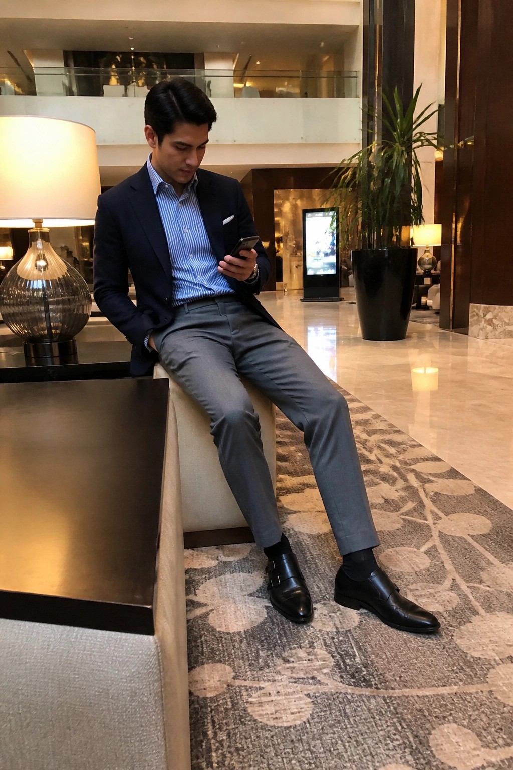 Man in navy blazer and gray trousers browsing smartphone in luxury lobby