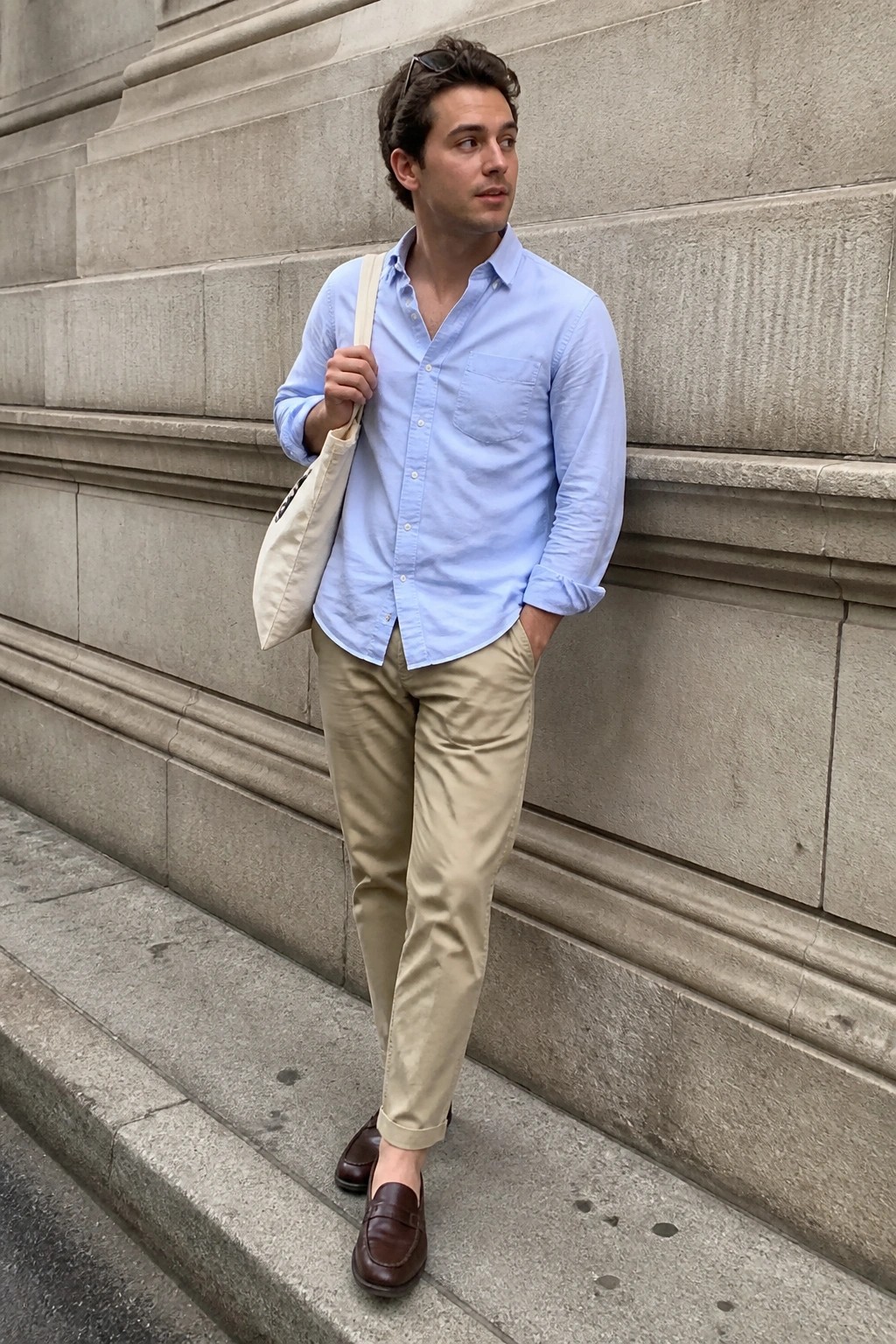 Man in light blue shirt and khaki pants with tote bag against stone wall