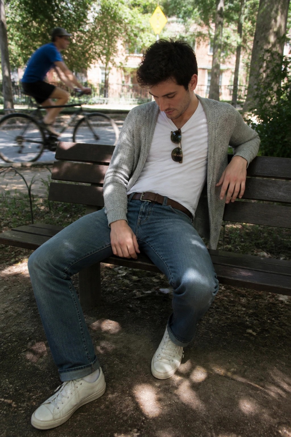 Man in white t-shirt, gray cardigan, and jeans seated on wooden park bench