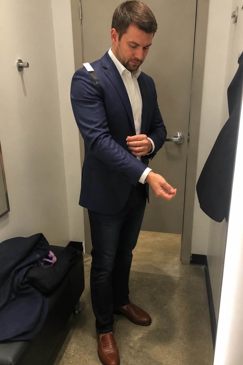 Man wearing navy blazer over white button down shirt with dark jeans and brown loafers in fitting room mirror selfie.