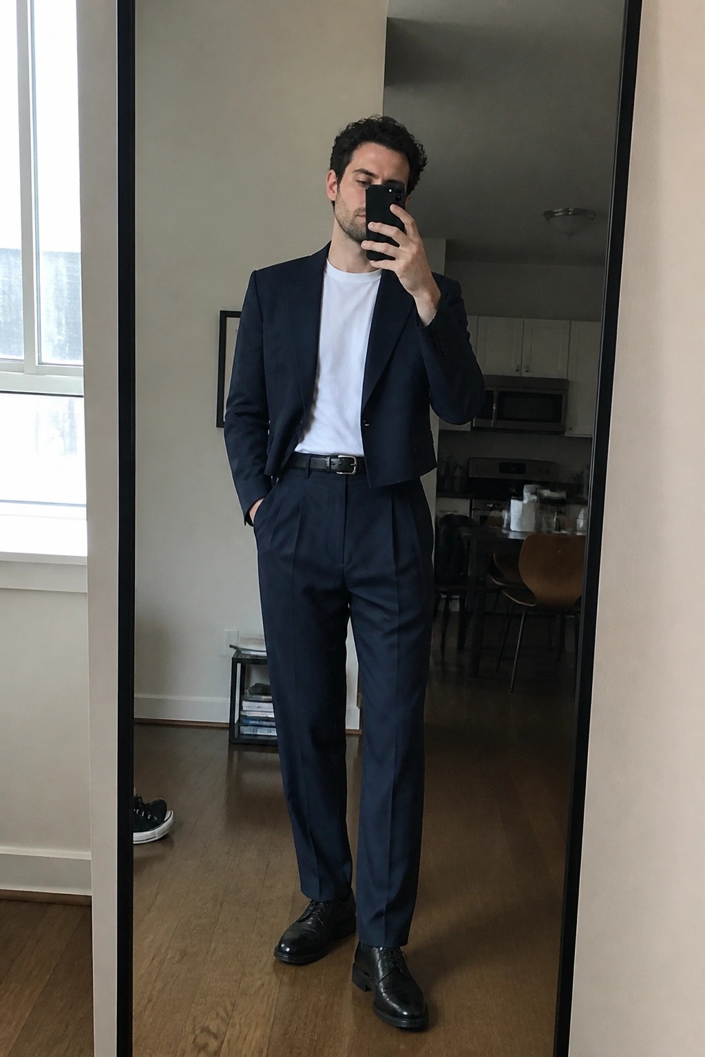Man in navy suit jacket and trousers over white t-shirt taking mirror selfie