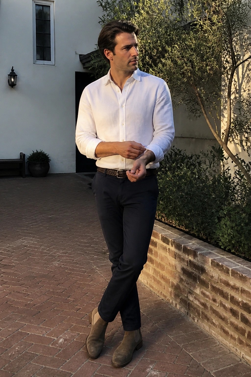 Man in white shirt and dark pants adjusting cuffs on brick patio