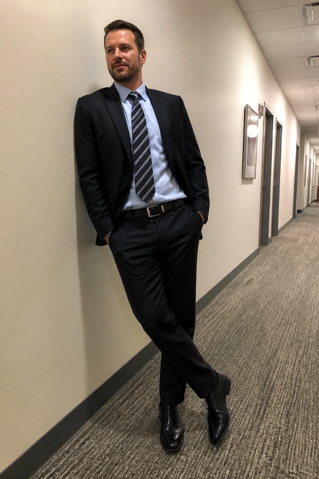 Man in black suit and light blue shirt leaning in office hallway