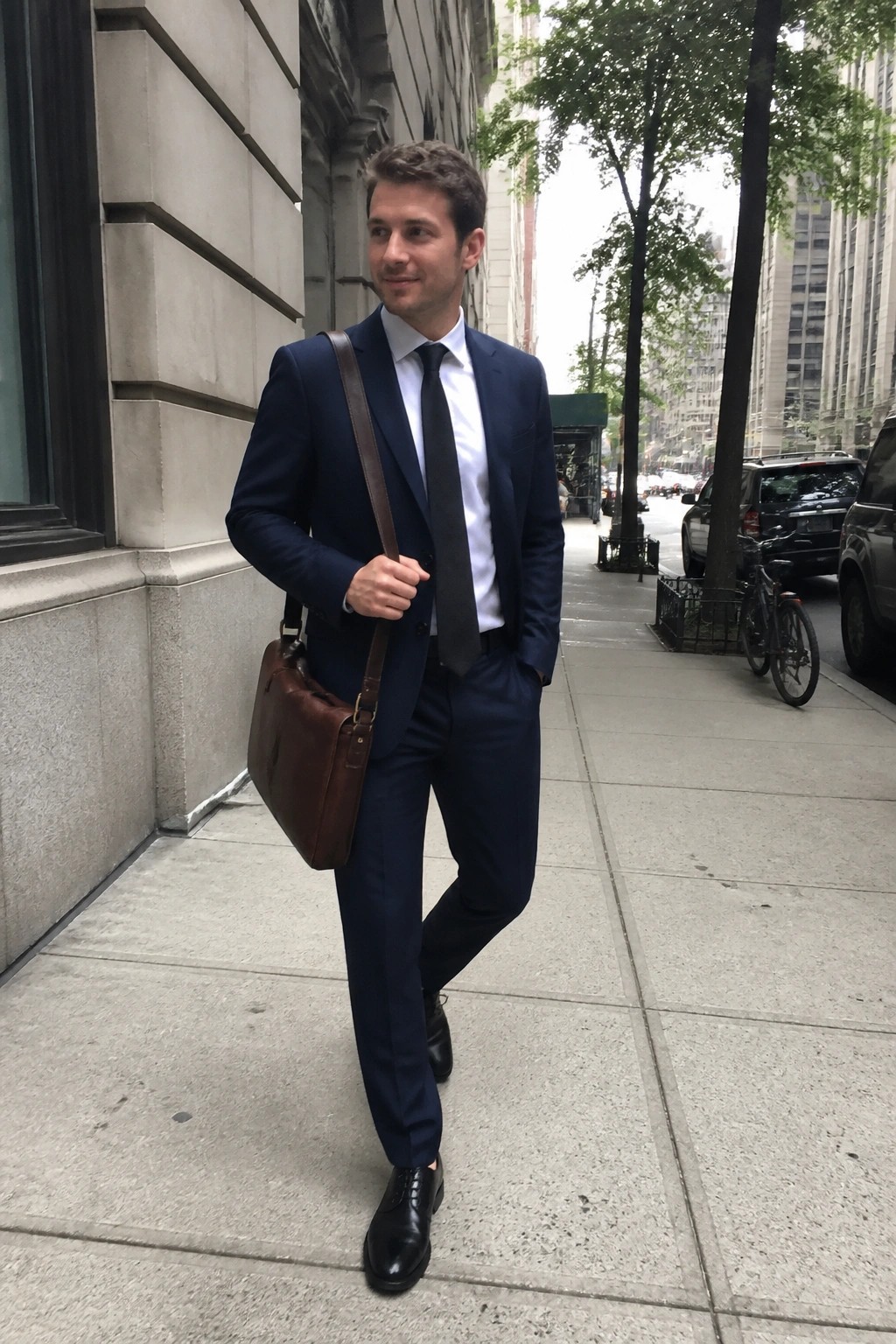 Man in navy suit with brown leather bag on urban sidewalk