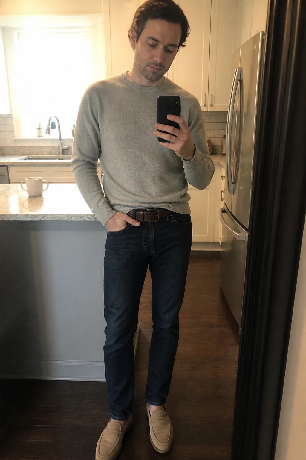 Man in gray sweater and dark jeans holding phone in modern kitchen