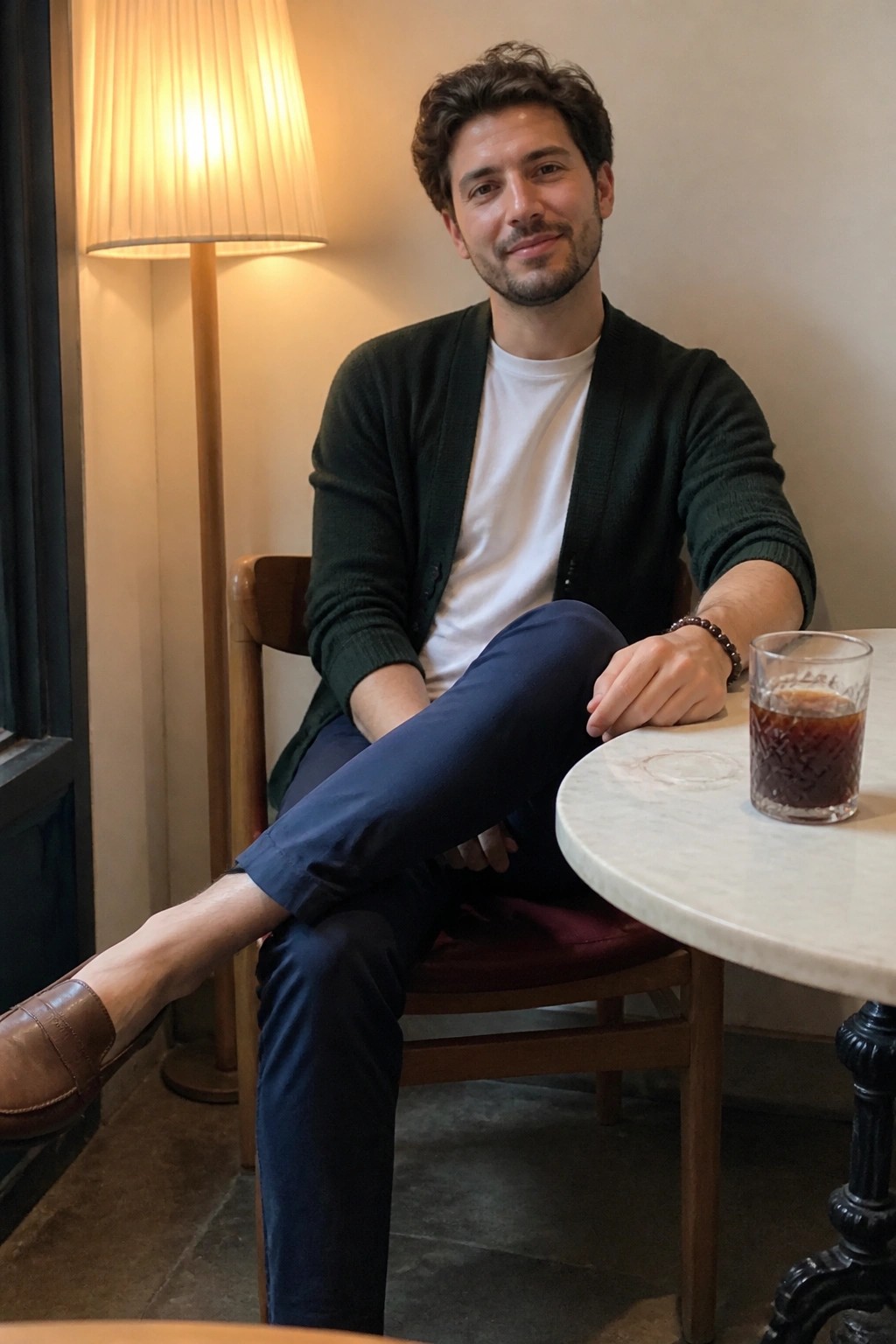 Man in green cardigan and blue pants at marble table with drink
