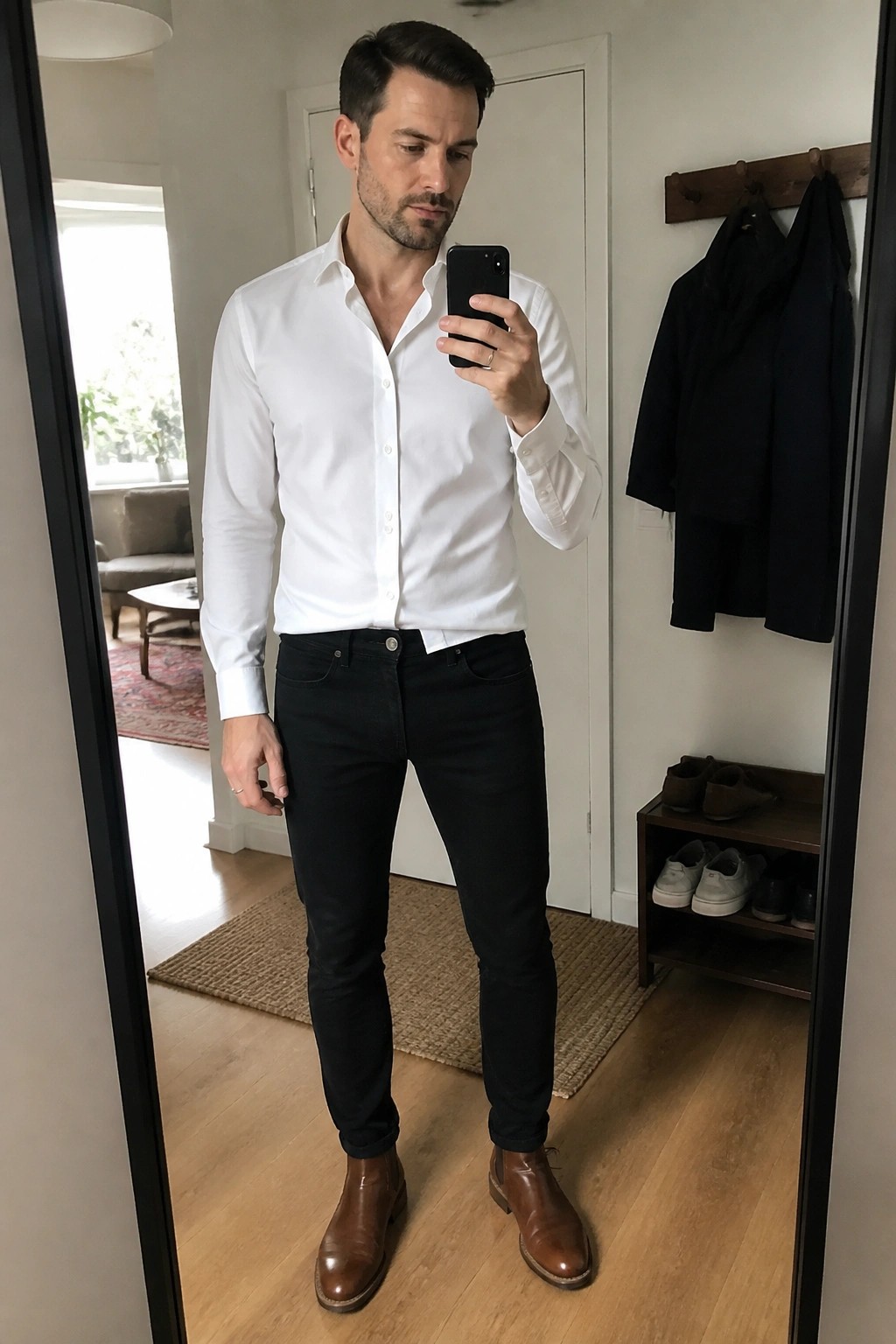 Man in white button-down shirt and black jeans taking mirror selfie in brown boots.