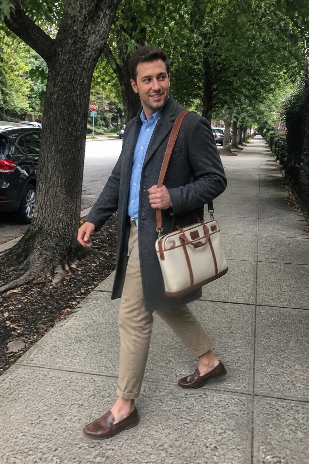 Man in gray overcoat and blue shirt carries white briefcase on sidewalk