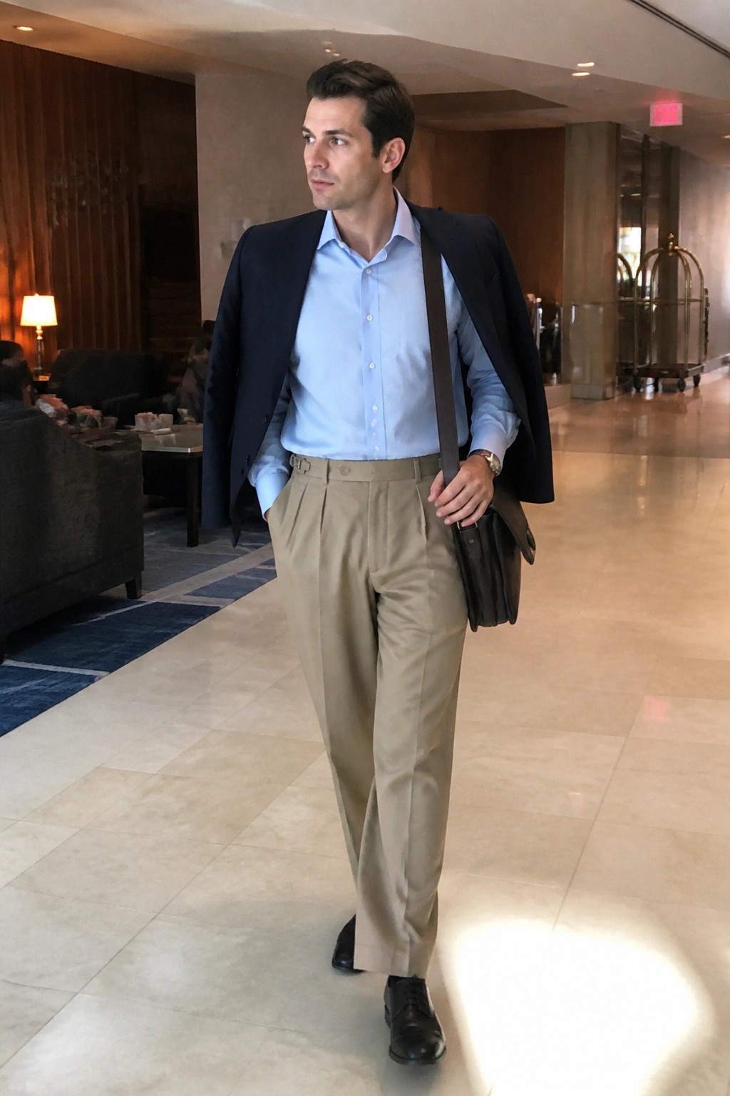Man in light blue shirt and blazer carrying bag walks in lobby