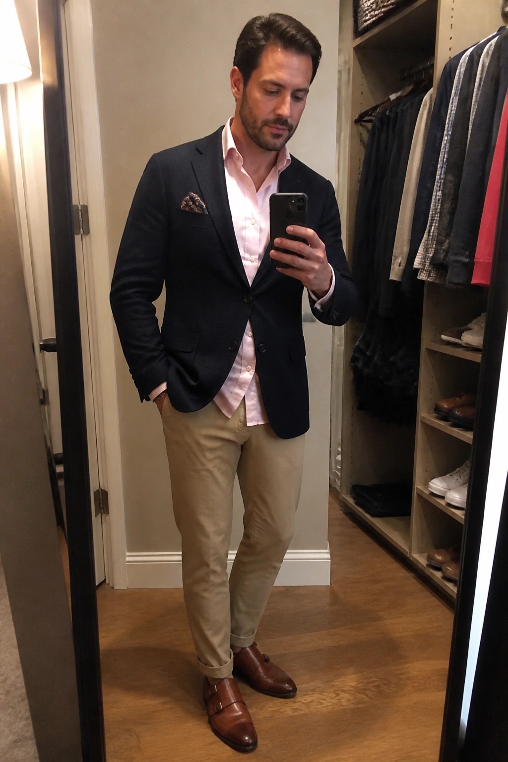 Man in navy blazer and pink shirt taking mirror selfie in closet