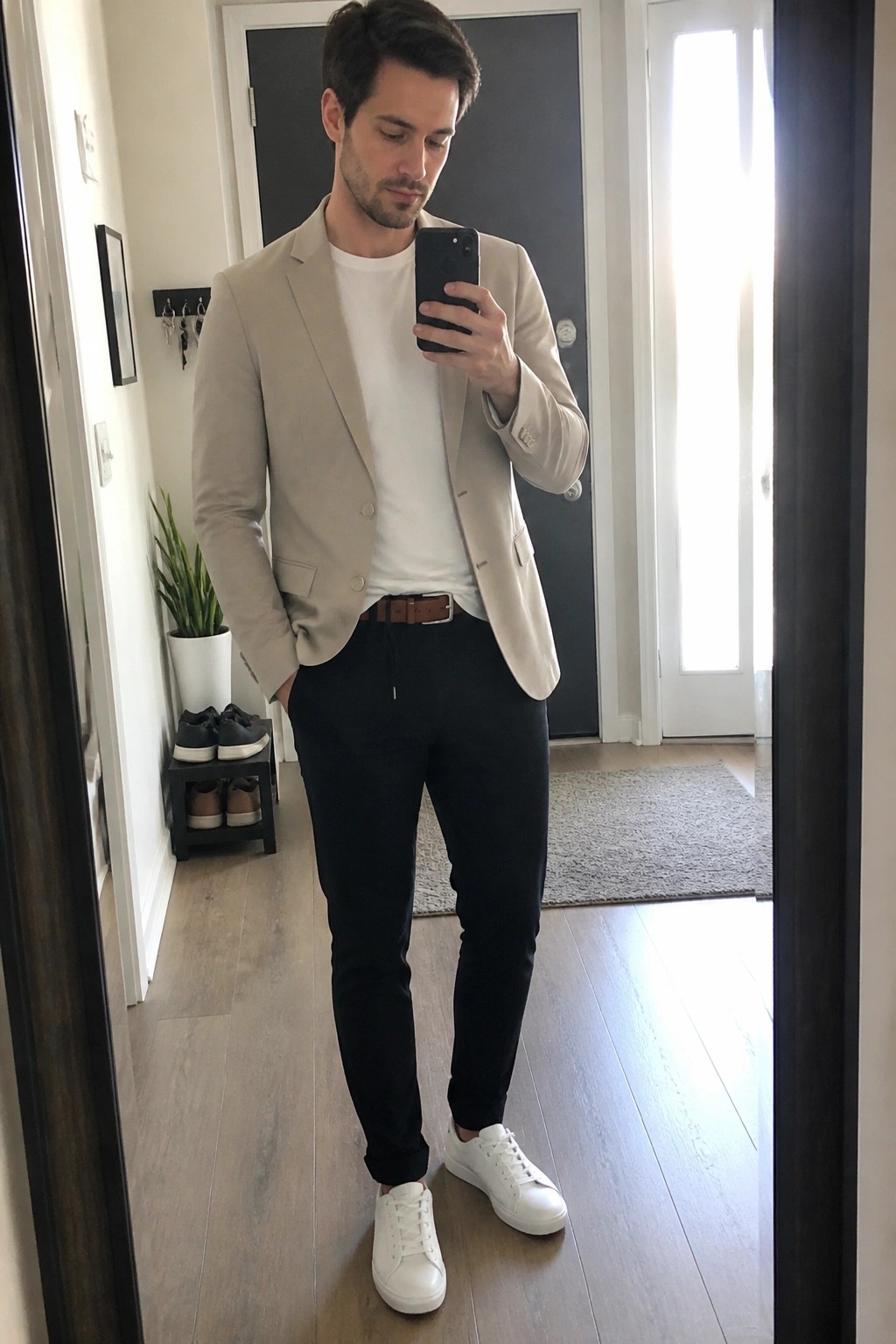 Man in beige blazer taking mirror selfie wearing black pants and white sneakers