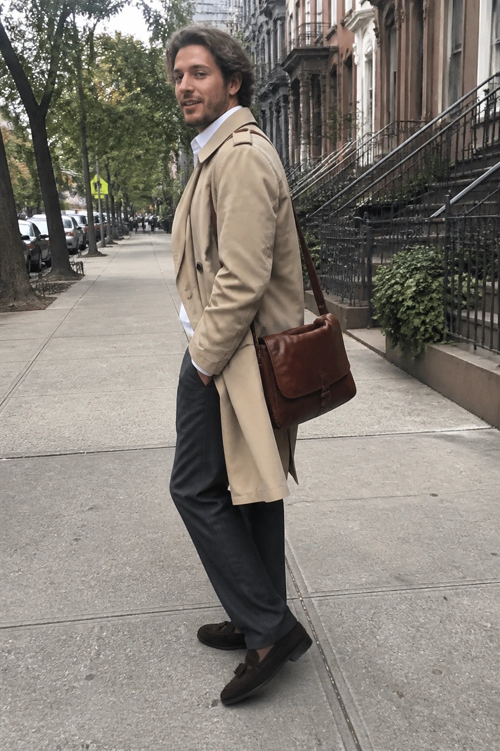 Man in beige trench coat with brown leather bag on city sidewalk