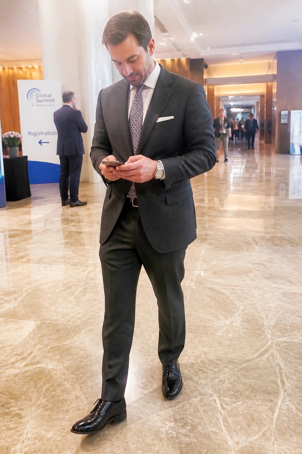 Man in dark suit checks smartphone on polished marble floor in lobby