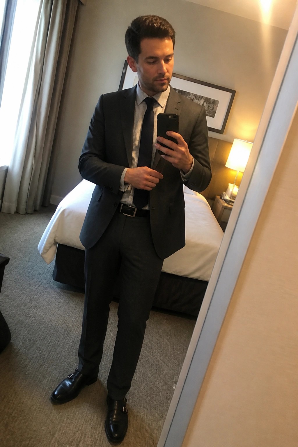 Man in dark gray suit taking mirror selfie in hotel room