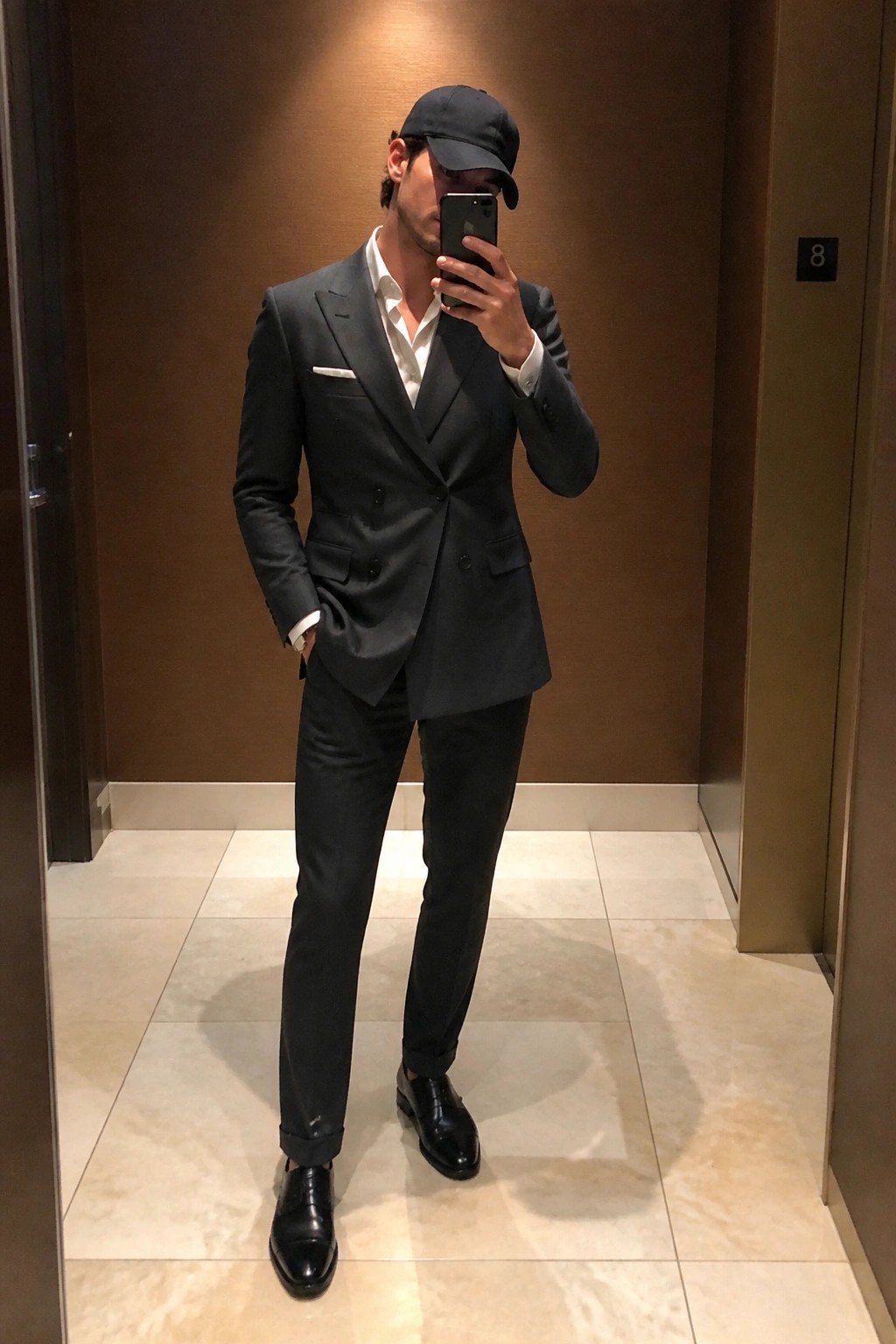Man in dark double-breasted suit and cap taking mirror selfie with phone