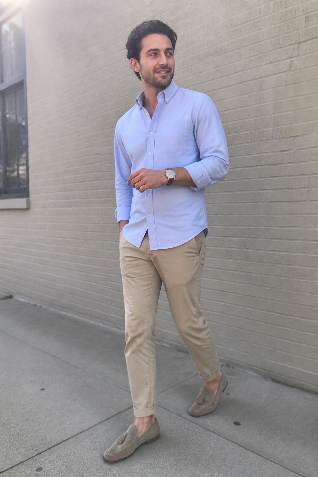 Man in light blue shirt and khaki pants standing against brick wall outdoors