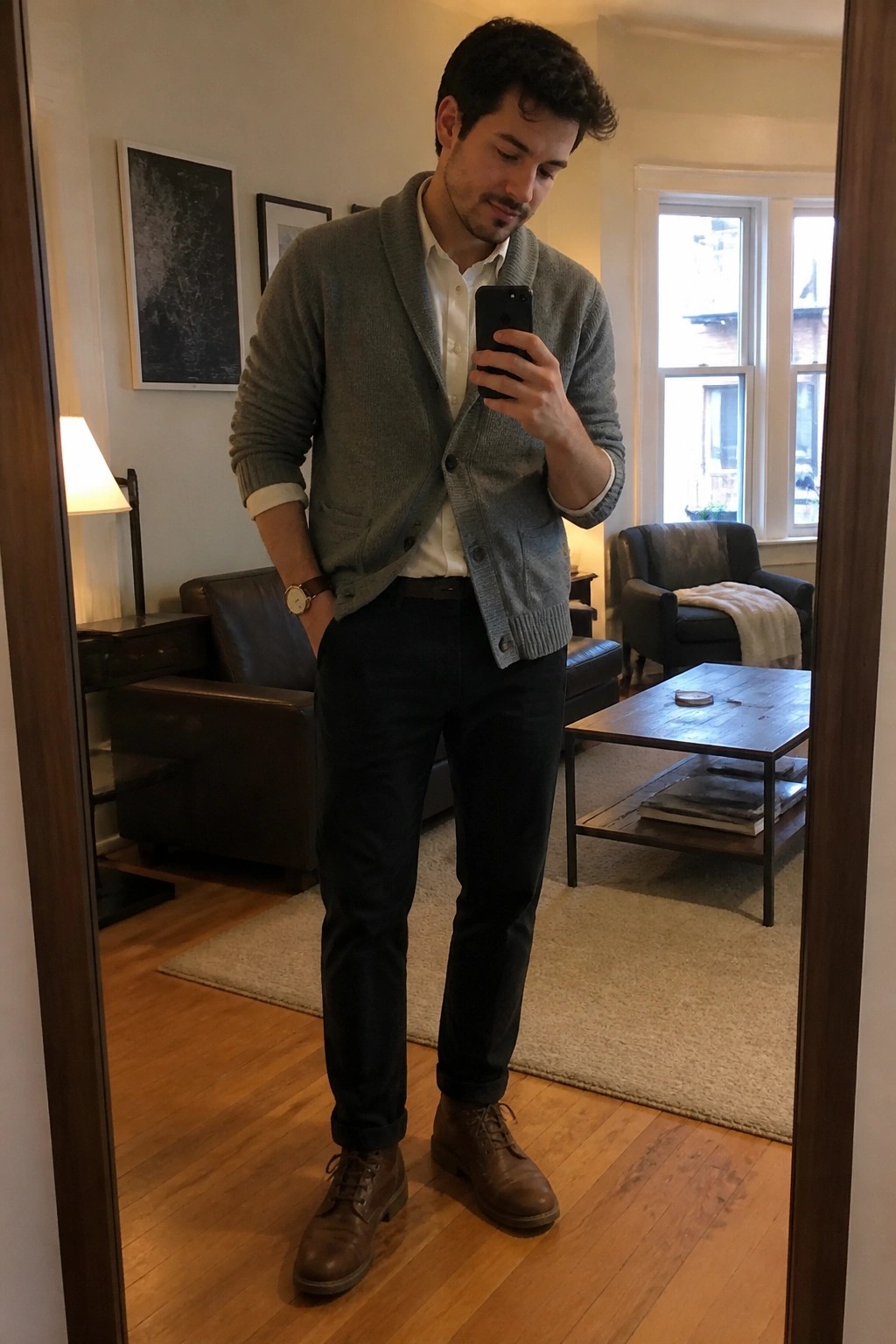 Man in mirror selfie wearing gray knit cardigan over white button down shirt with dark trousers and brown lace up boots