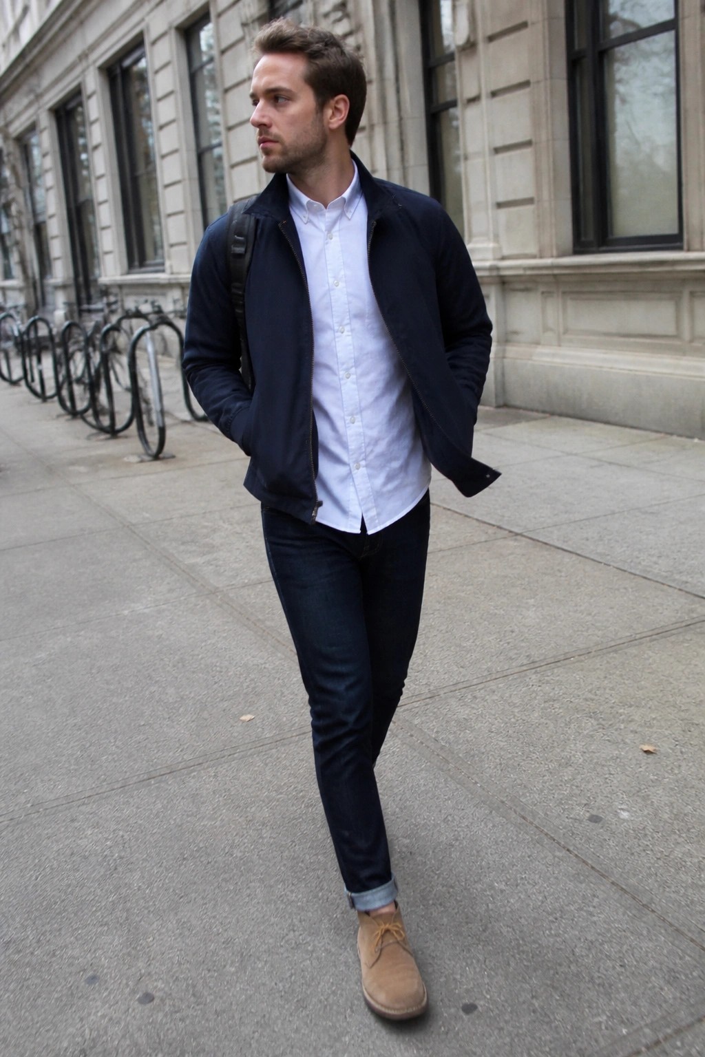 Man in navy jacket over white shirt with backpack walks on city sidewalk
