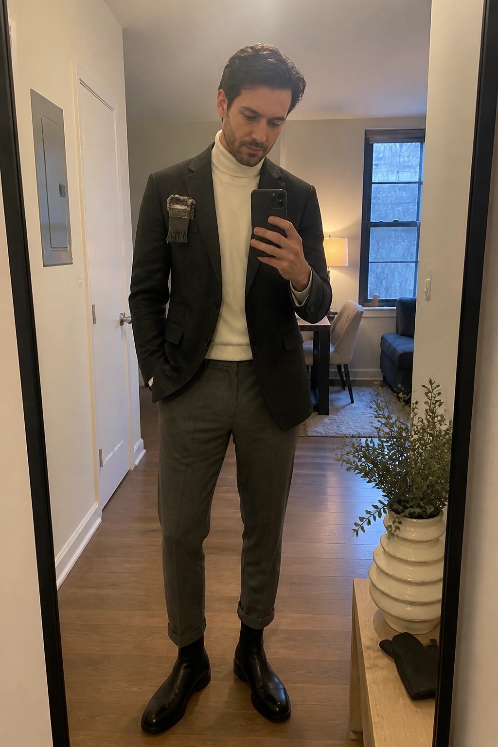 Man in dark blazer over white turtleneck taking mirror selfie with gray pants and boots