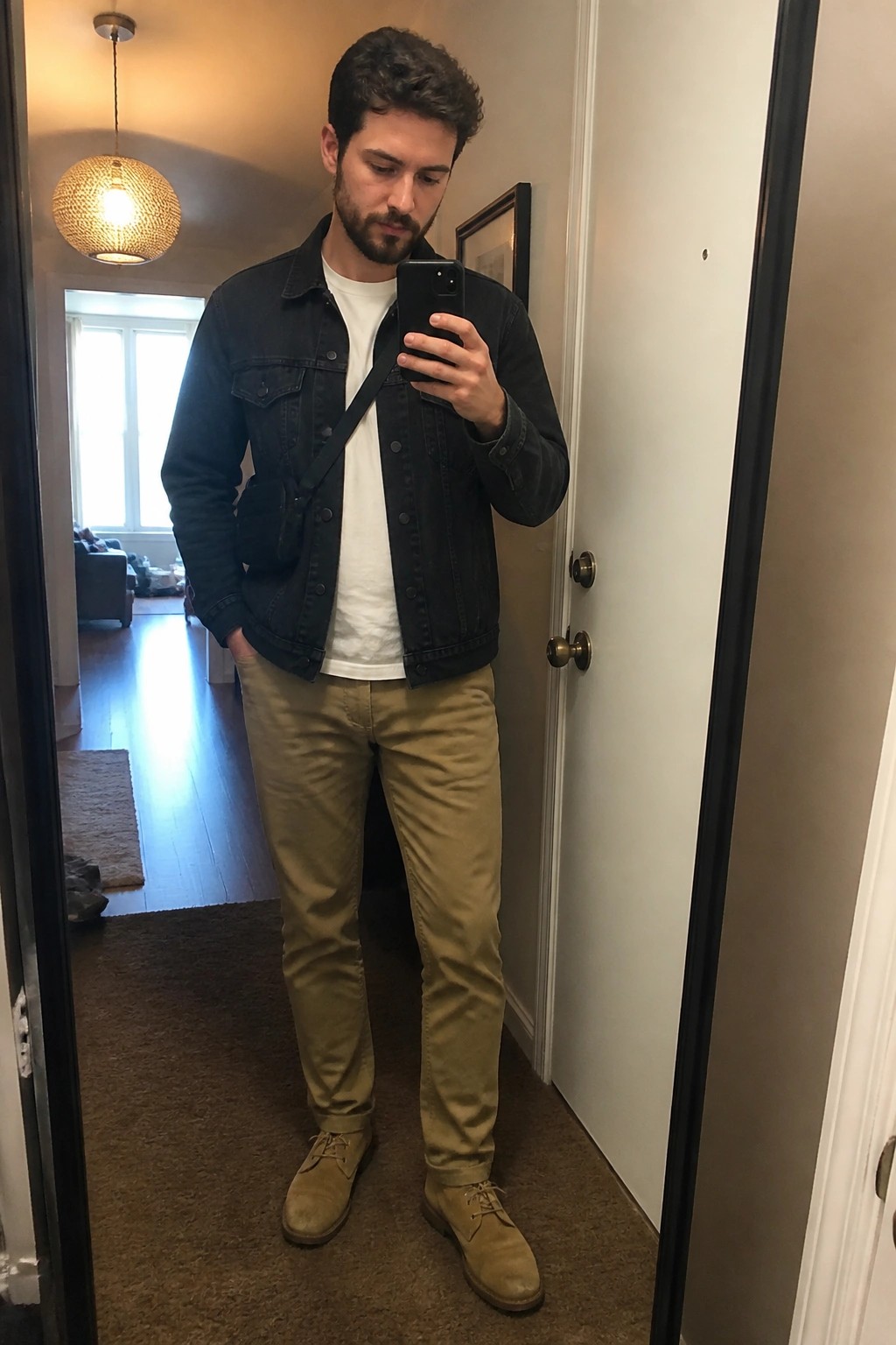 Man in denim jacket and khaki pants taking mirror selfie in hallway