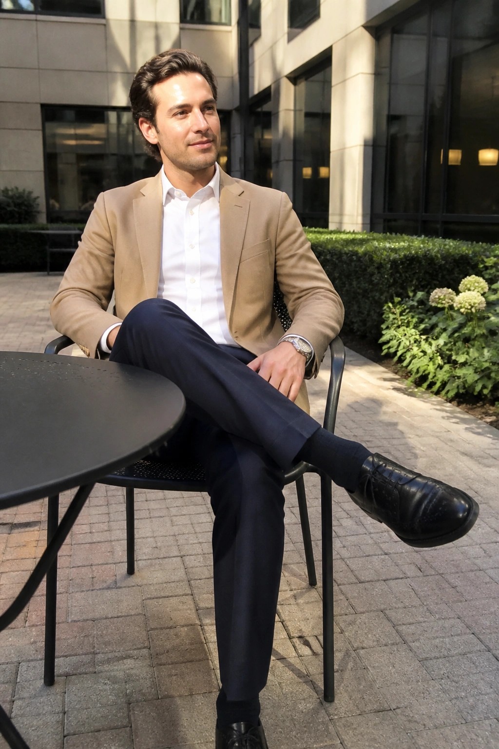 Man in tan blazer and white shirt sits with legs crossed at outdoor table