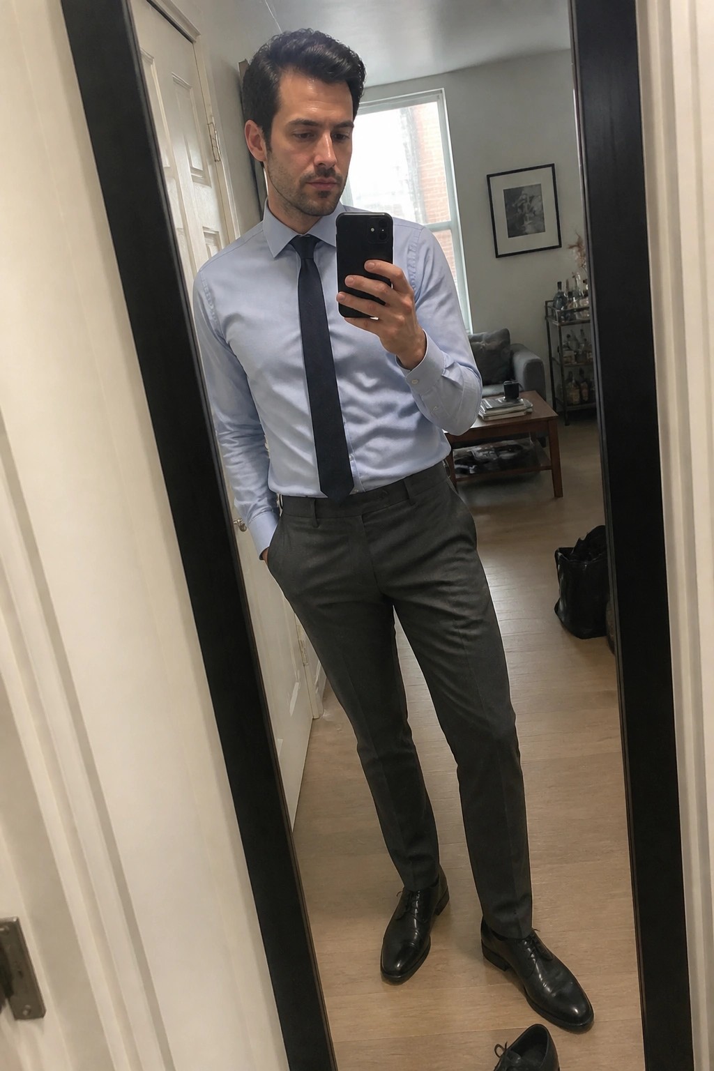 Man in light blue shirt and gray pants taking mirror selfie with phone
