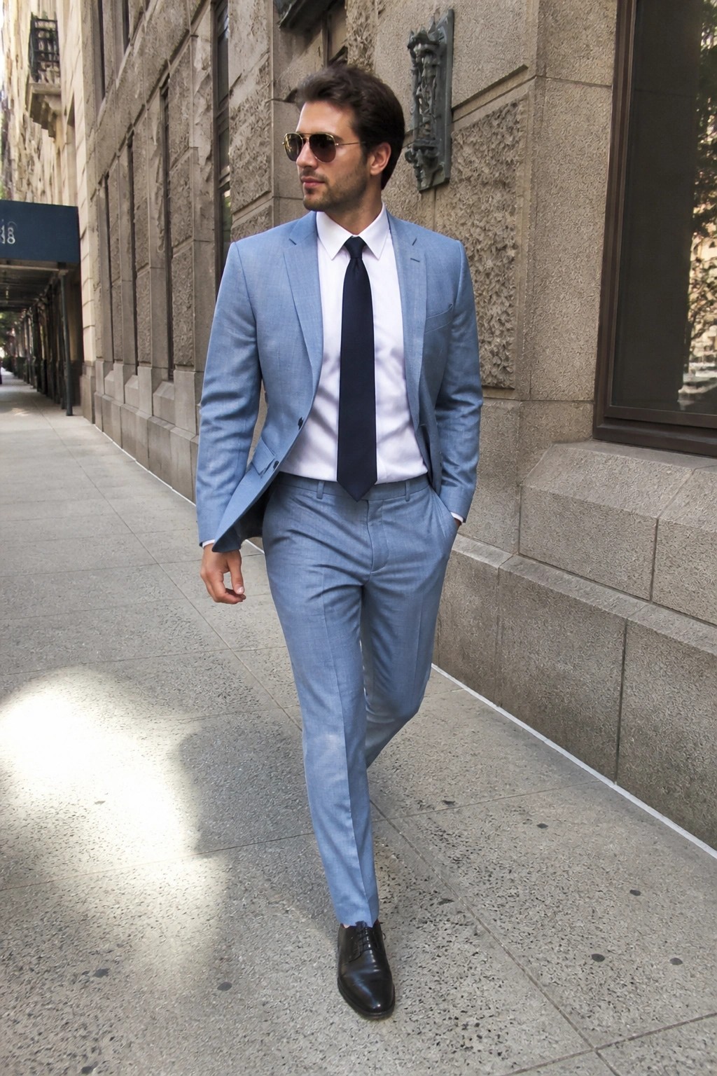 Man in light blue suit, white shirt and navy tie on city sidewalk
