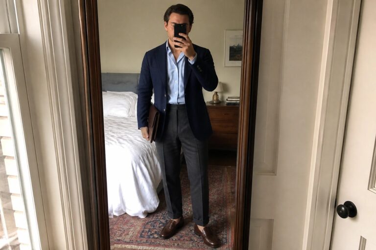 24 Smart Business Professional Outfits for Men Who Value Comfort and Structure Man in navy blazer and light blue shirt holding brown leather portfolio in bedroom mirror
