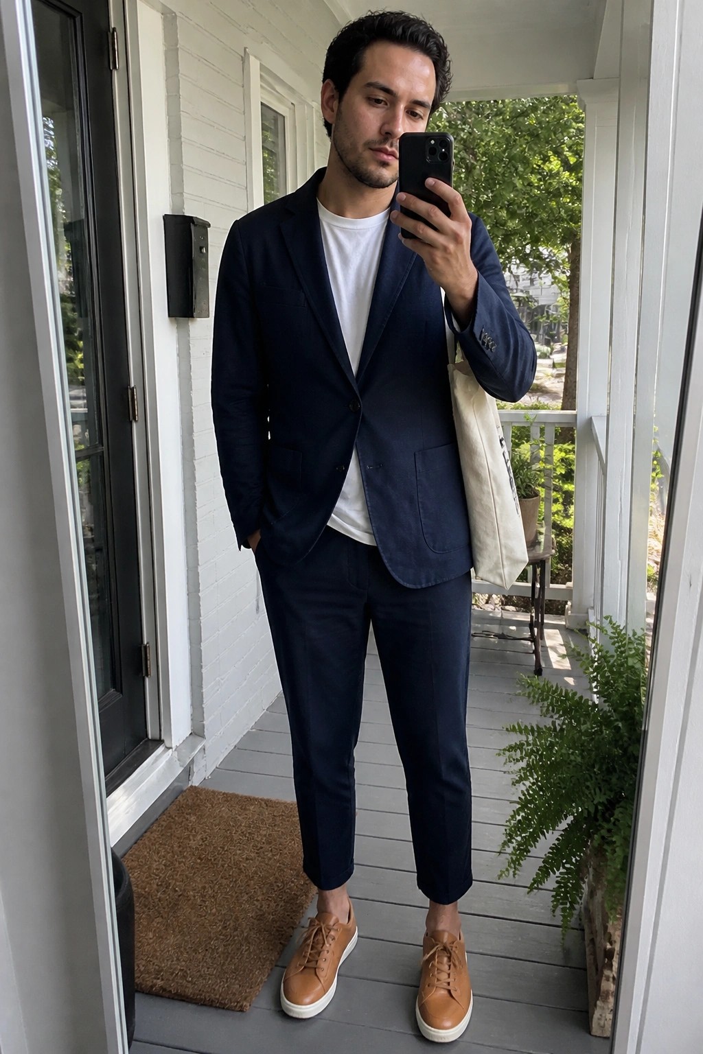 Man in navy blazer and pants taking selfie on porch with tote bag