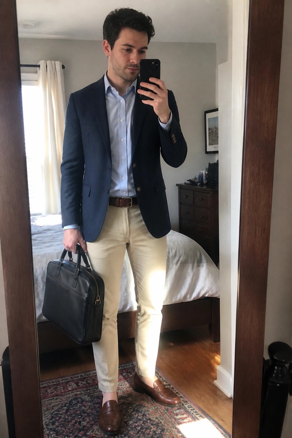 Man in navy blazer and khaki pants taking mirror selfie while holding briefcase