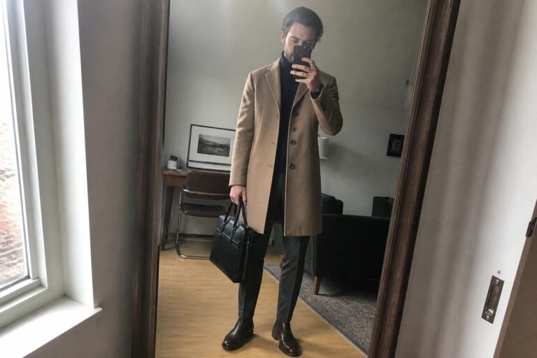 24 Warm Winter Office Outfits for Men That Stay Professional in Cold Weather Man in tan overcoat and navy turtleneck holding black briefcase in mirror selfie