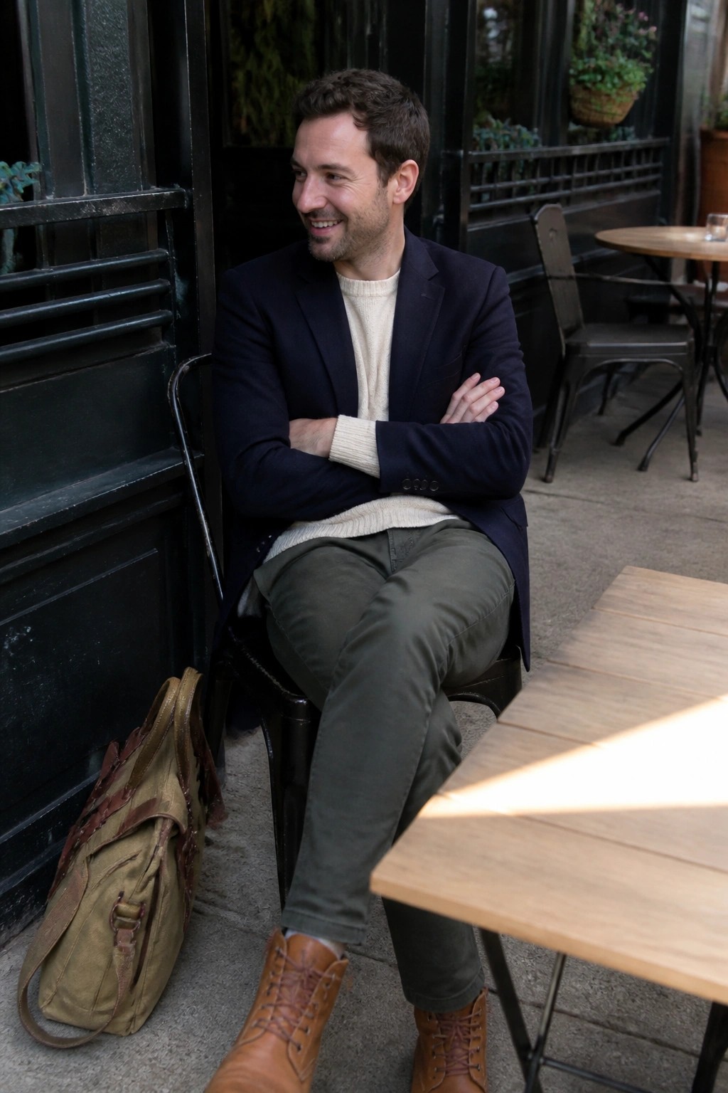 Man in navy blazer and cream sweater sits with arms crossed at cafe