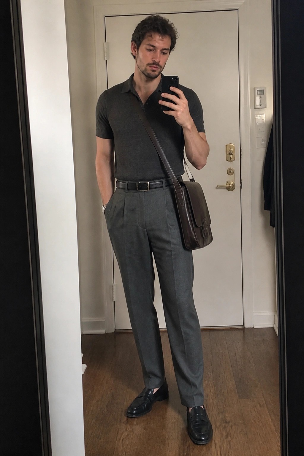 Man in gray polo shirt and pleated trousers with brown leather messenger bag