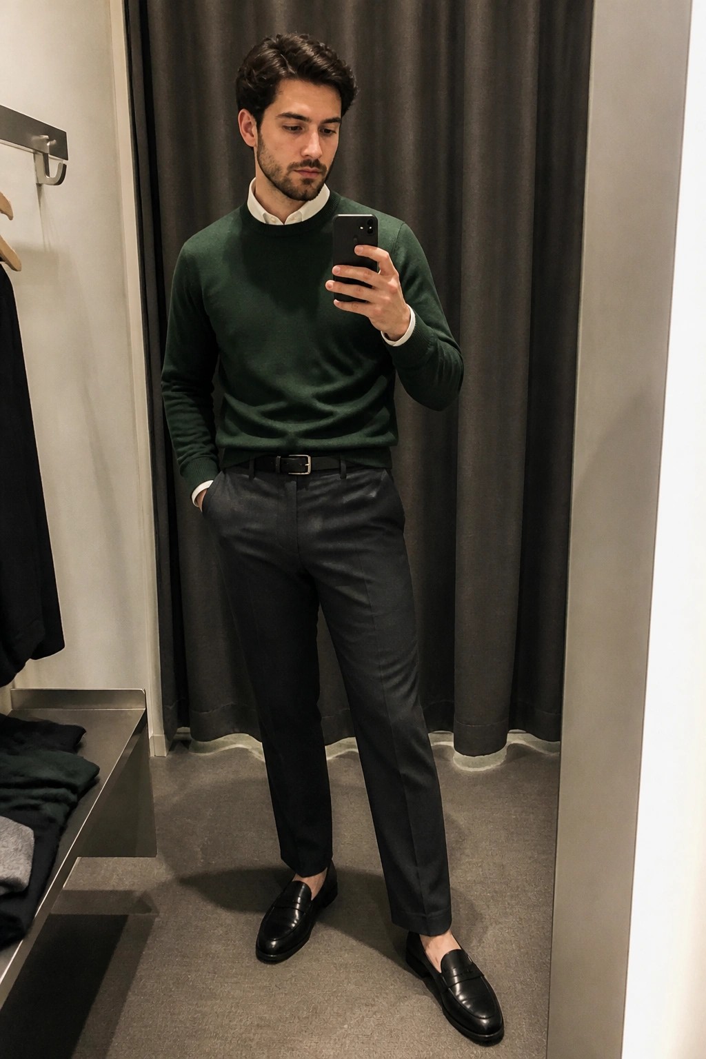 Man in green sweater taking mirror selfie while wearing black loafers and trousers