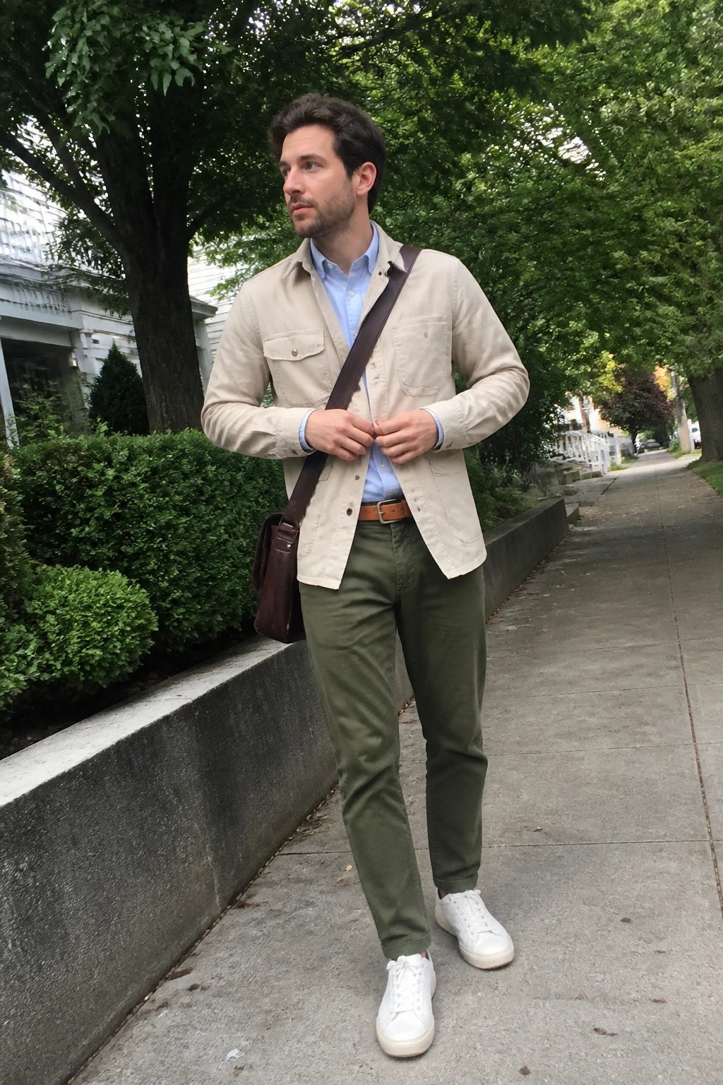 Man in beige jacket, blue shirt, green pants, and white sneakers on sidewalk