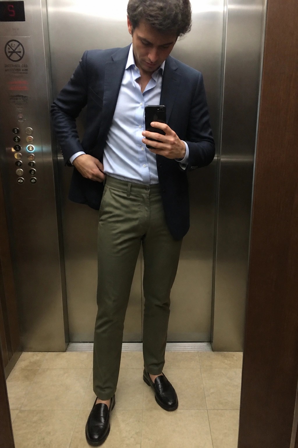 Man in navy blazer and olive pants taking selfie in elevator
