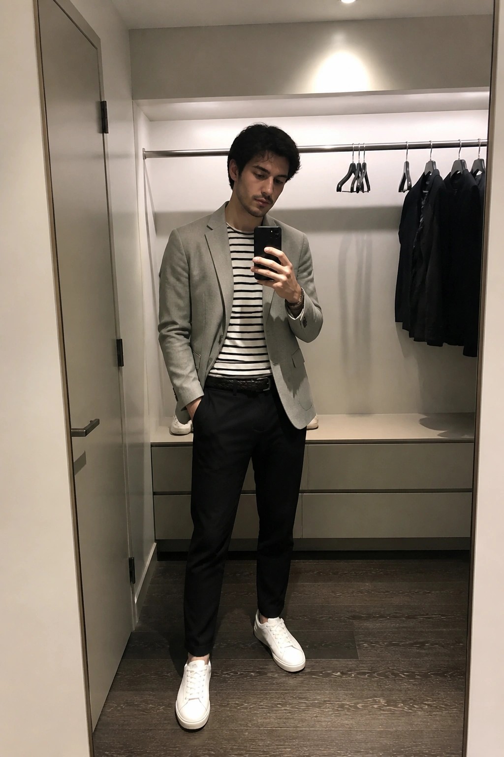 Man in gray blazer over striped shirt taking mirror selfie in closet