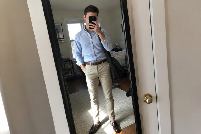 25 Practical First Office Job Outfits for Men Building a Versatile Work Wardrobe Man in light blue shirt and khaki pants taking mirror selfie with bag